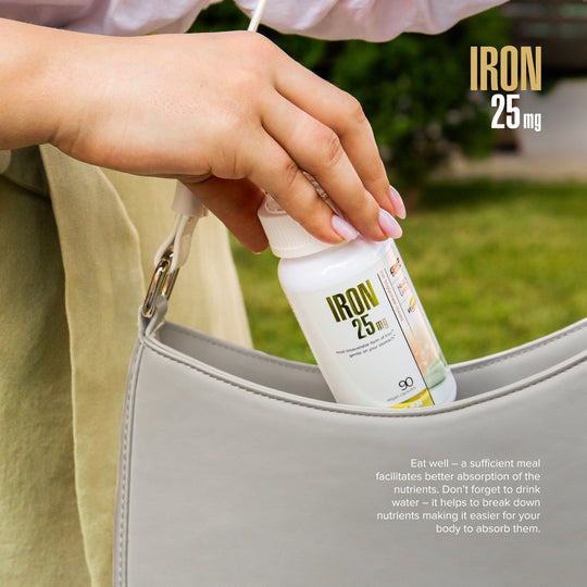 Person placing a supplement bottle labeled 'IRON 25 mg' into a handbag with a green outdoor background.
