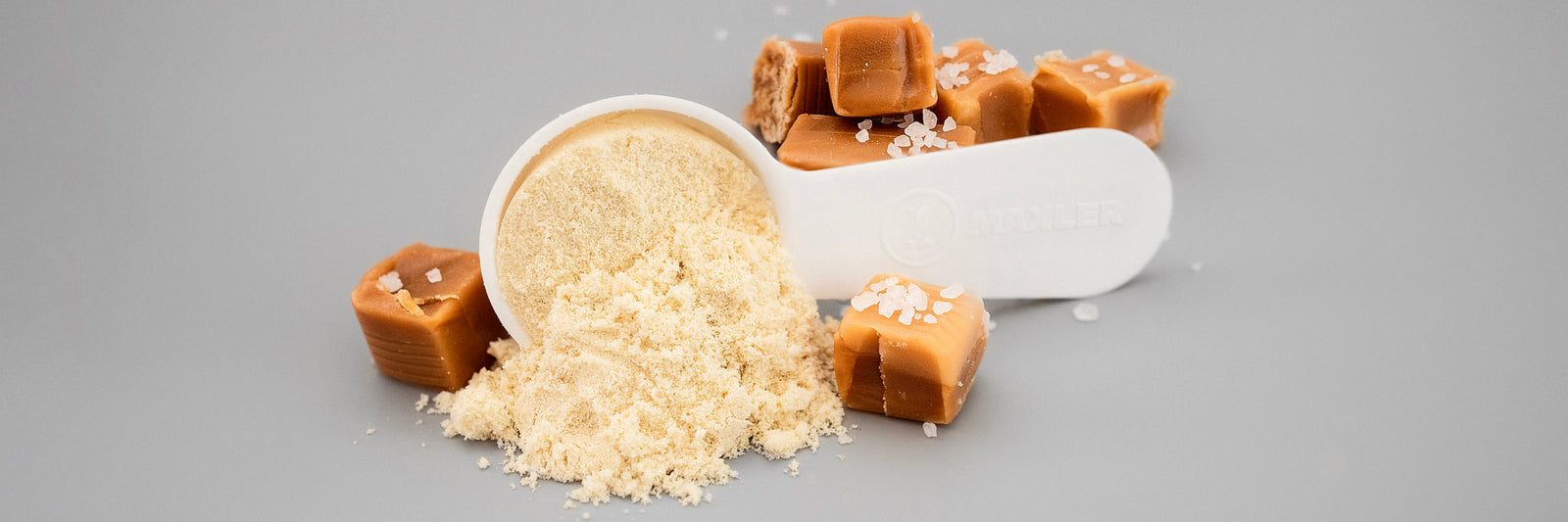 Hydrolysiertes Molkenproteinpulver mit Messlöffel und Karamellstückchen